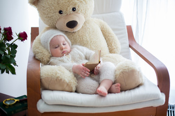 Sweet little baby boy, sleeping with huge teddy bear in big armchair