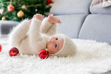 Little baby boy in white knitted onesie, playing with and opening presents at home © Tomsickova