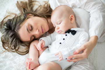 Mother and her baby son, sleeping on a big bed, soft back light