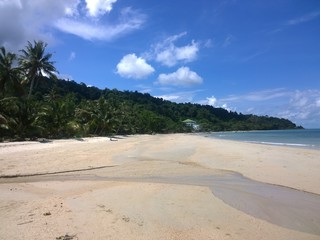 Blue sky and clouds over a tropical beach with green palm trees on Koh Chang island in Thailand