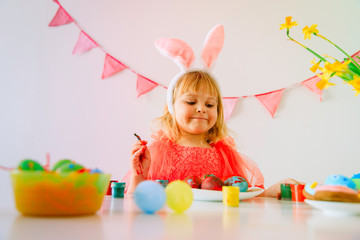 happy little girl painting eggs for easter