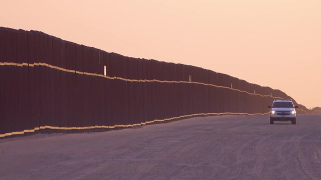 Border patrol vehicle watches near the border wall at the US Mexico border at Imperial sand dunes, California.