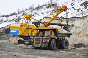 Excavator loads dump truck in quarry in winter