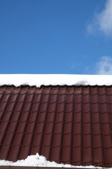 Side of country house roof from brown metal tile with snow in sunny spring day under blue sky with white clouds vertical front view