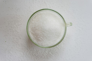 Close up of a glass of white sugar, a white wooden rustic table, shallow depth of focus.
