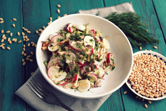 Quail eggs salad in the white bowl. Healthy lunch. European cuisine. Close up. Radish, cucumber, quail eggs and pine nuts. Ovo vegetarian dish. Top view.