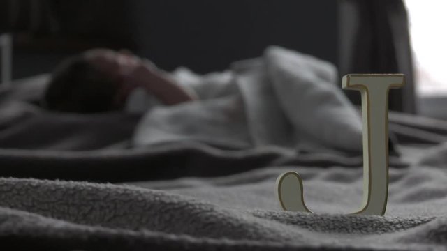 newborn baby sleeps with letter J in foreground in focus