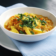 Red lentil stew with potato, carrot and turmeric. Toned photo. Healthy lunch on the round white plate. Colorful vegan dish with potato, carrot and turmeric. European cuisine. Vegetarian.