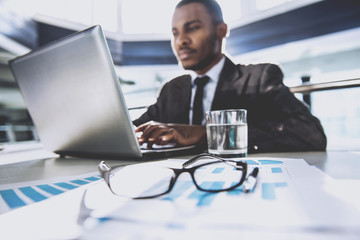 Young black businessman is sitting at the table and working, in modern office