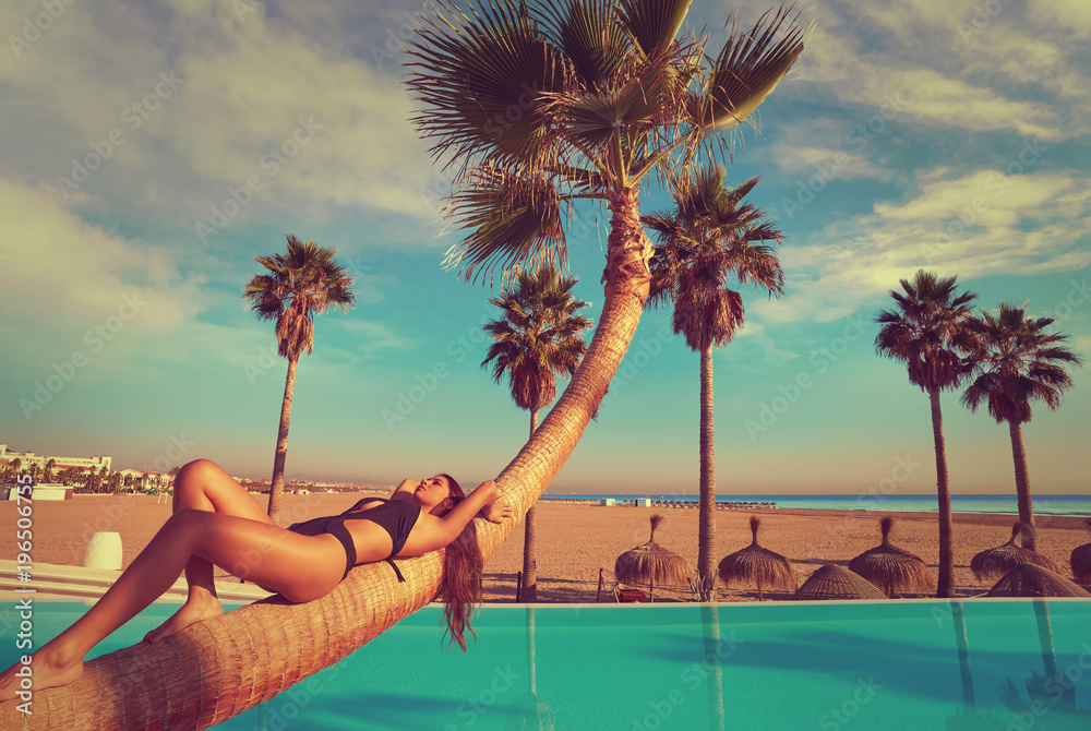 Wall mural woman lying on pool bent palm tree trunk