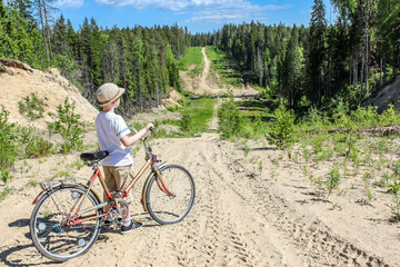 Traveller boy with a bicycle stands on a road descending from the mountain in the summer