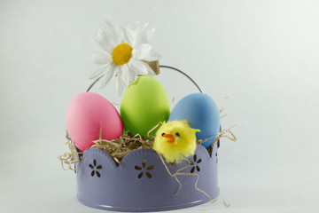 Easter background with basket, straw, yellow chick, daisy and 3 colored eggs