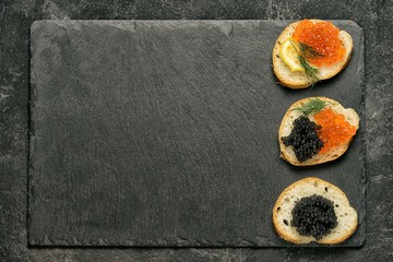 sandwiges with red salmon caviar and black stugeon caviar on a black stone board on a black table,...