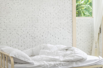White bedding sheets and pillow in white room background. Messy bed concept in moring time.