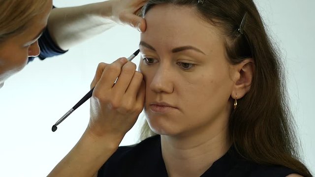 Eye makeup woman applying eyeshadow powder. Stylist is doing make up for female by eyeliner