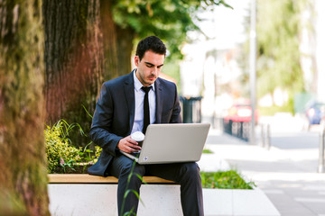 Young businessman use laptop while siiting on the bench at the avenue