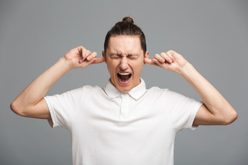 Screaming young man standing isolated covering ears.
