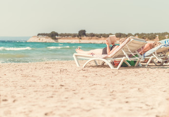 Woman lying on sun lounger by the sea reading a book at the beach on a sunny day
