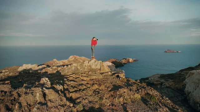 Aerial footage of drone flying around professional female photographer, empowered and independent, taking risks and adventures to find success and perfect shot on high mountain peak