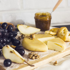 Cheese, honey, grapes, pears and nuts on wooden board on kitchen