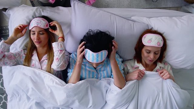 Top view, three beautiful girls go to sleep on the bed and put eye bandages to sleep.