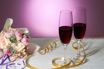 Beautiful wedding bouquet of pink roses wih red wine glasses on a white wooden background