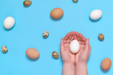 Woman holding white egg in hands with eggs on blue background, copy space. Healthy food concept. Top view, flat lay. Easter eggs. Happy Easter concept