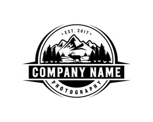 Obraz premium Beautiful Deer Animal on the Park Pine Tree with Mountain Silhouette Symbol Vintage Circle Logo Vector