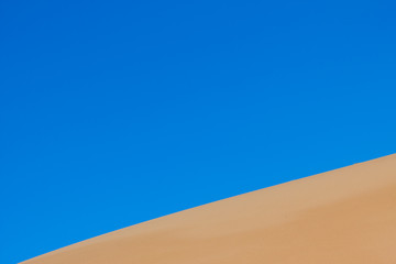 Yellow sand dunes and blue sky in the desert. Negev in Israel. The dunes look like giant waves crossing the sky. 
