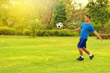Asian man playing football alone in garden
