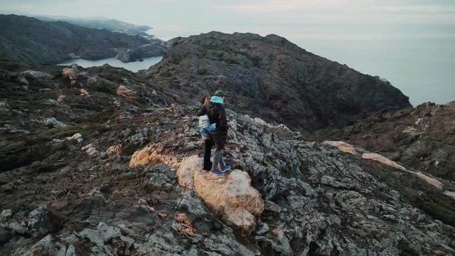 Amazing epic drone shot over breathtaking landscape of cliffs, rocks, mountains and sea or ocean.Young couple of nomads, adventurers or travel inspiring bloggers stand together on edge and enjoy views