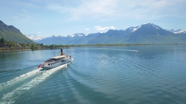 4K Switzerland iconic aerial shot of boat cruise on the lake. Following a vintage boat on Lake Geneva, with the Alps in the background