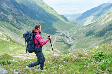 Hiking trip in the mountains of Romania. Girl with a backpack and trekking sticks on a blurred background of a picturesque landscape most beautiful road in Europe - Transfagarashan Highway