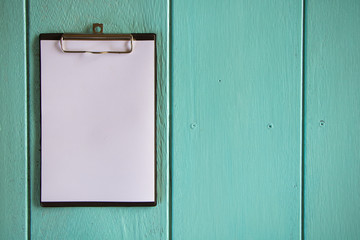 Clipboard with white sheet on wood background. Top view.Vintage style.