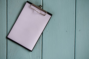 Clipboard with white sheet on wood background. Top view.Vintage style.