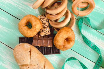 fruit with Cup of yogurt and bread separated by a measuring tape with chocolate and donuts on a green wooden background, concept of proper nutrition