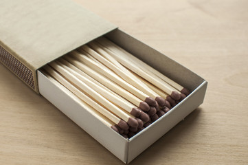 Long wooden safety matchsticks stacked in cardboard matchbox on wooden background