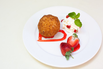 Fried ice cream with whipped cream and strawberry on plate.