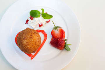 Fried ice cream with whipped cream and strawberry on plate.