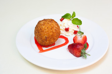 Fried ice cream with whipped cream and strawberry on plate.