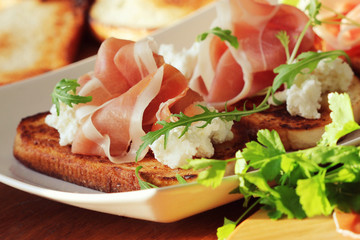 Bruschetta with ricotta, prosciutto, rucola on white plate