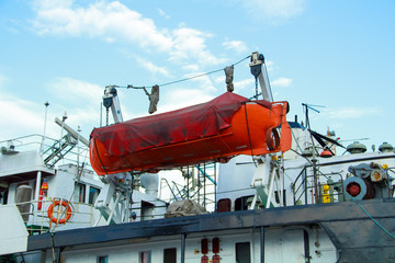 Orange lifeboat on a ship against the blue sky.