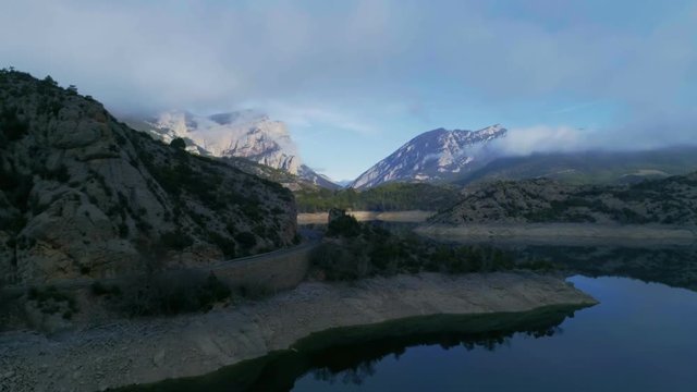 Aerial shot of sunrise in mountain. Drone moves on side to show wonderful parallax effect with moving mountains around lake. Sky is mirrored in clear quet water.