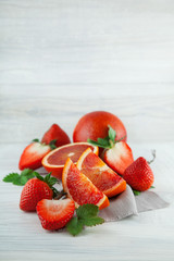 fresh ripe blood oranges and strawberries, slices, rustic food photography on white wood plate kitchen table can be used as background