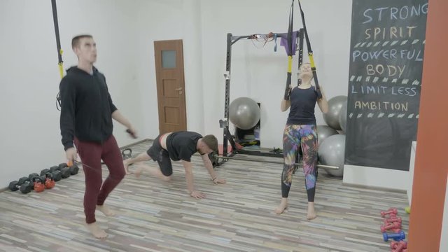Athletic man jumping rope fast near a determinated fitness girl who works out her arms in a small gym