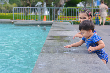 Naklejka premium Little latin sibling playing near to waterpool. 