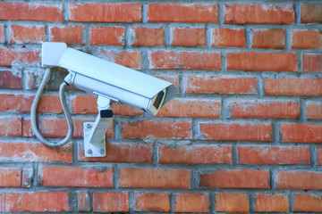 Stationary outdoor video camera in a thermal housing of a security video surveillance system on a brick wall.