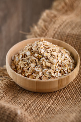 Dry rolled oatmeal in wooden bowl on textile background.