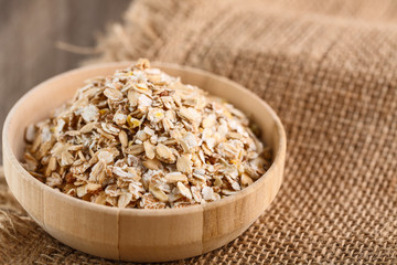 Dry rolled oatmeal in wooden bowl on textile background.