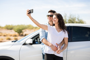 Happy couple taking selfie near car outdoors